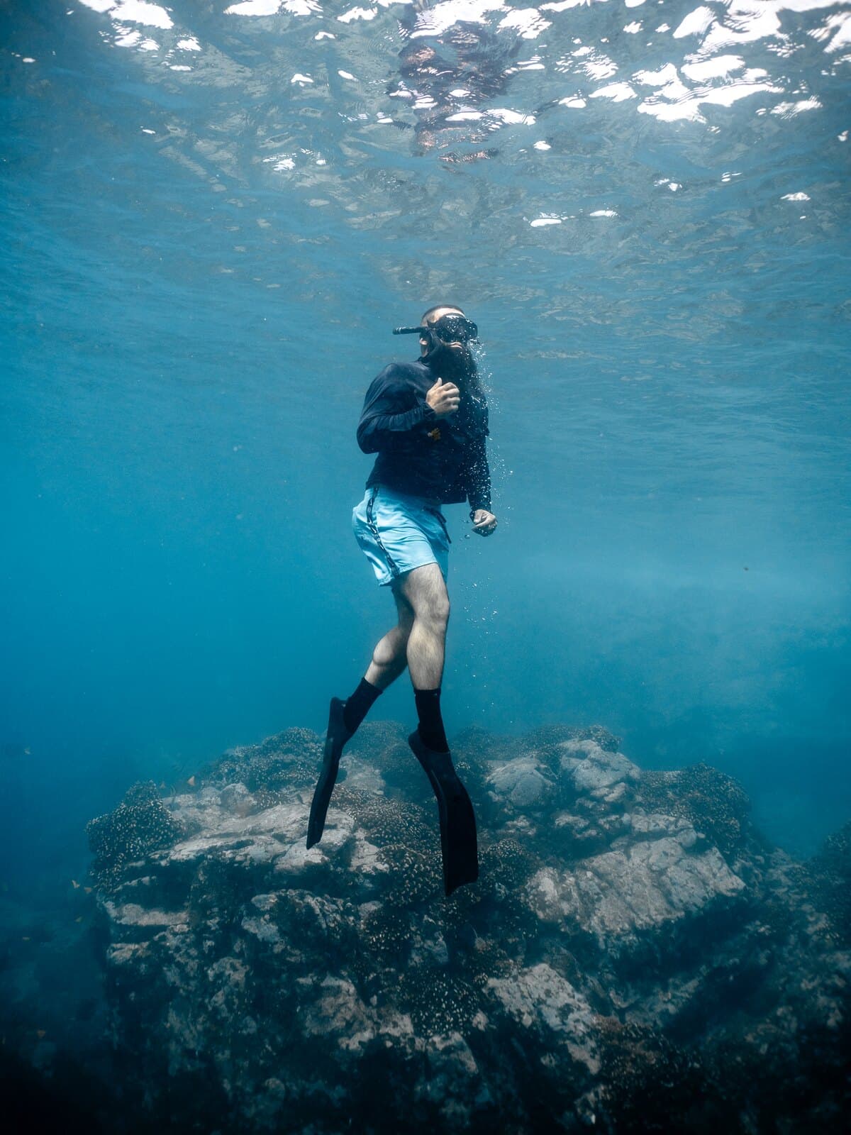 A freediver hovering upright above a rocky seabed