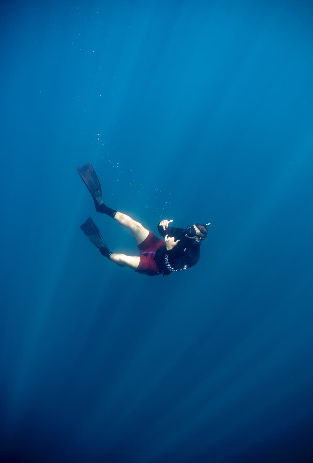 A freediver making a shaka sign in open blue water