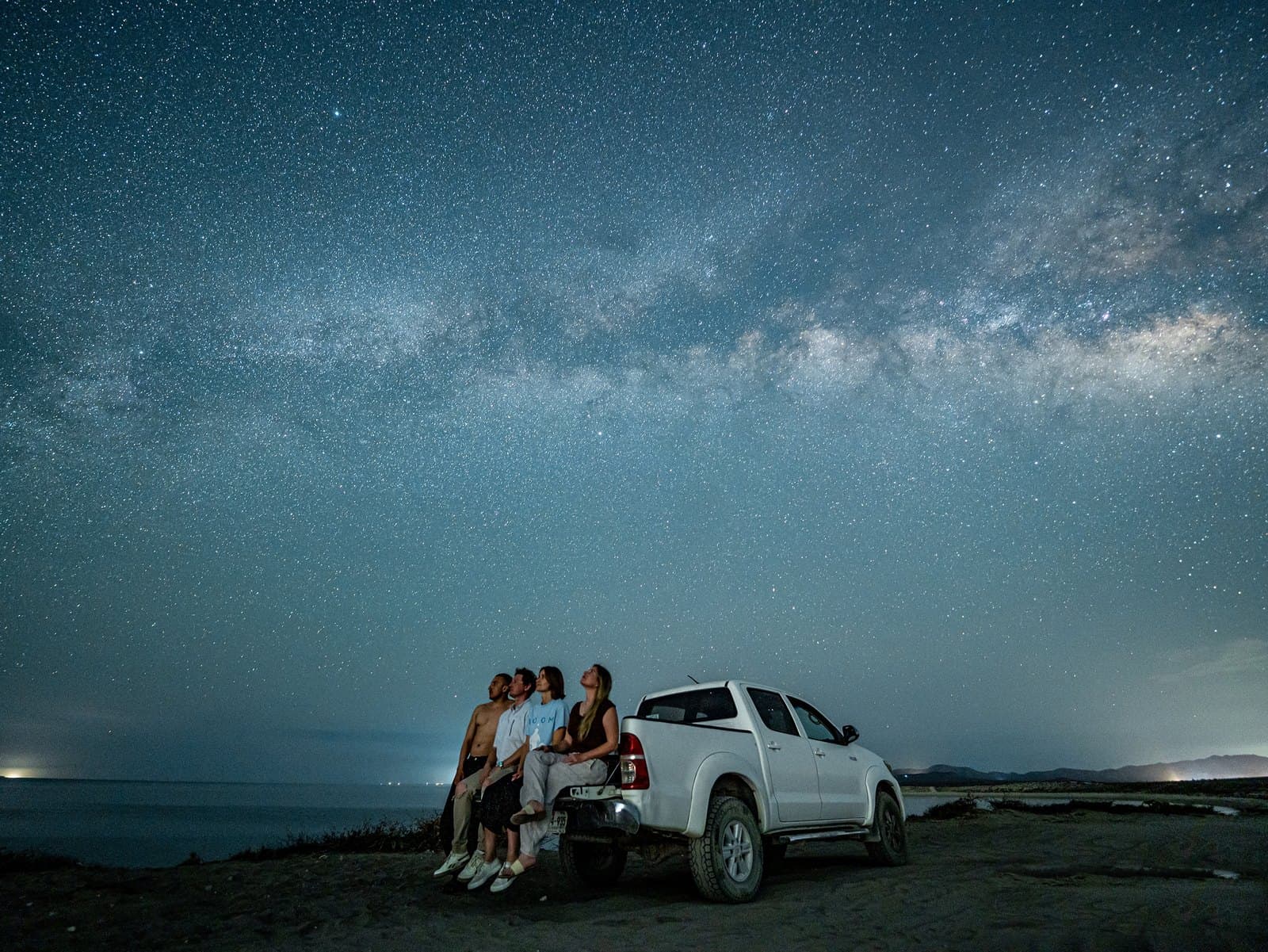 Four people beside a white pickup truck beneath the Milky Way