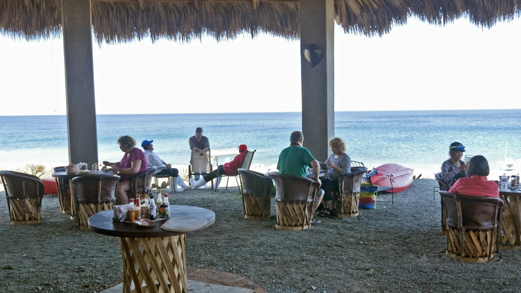 Guests seated for a meal beneath a waterfront palapa