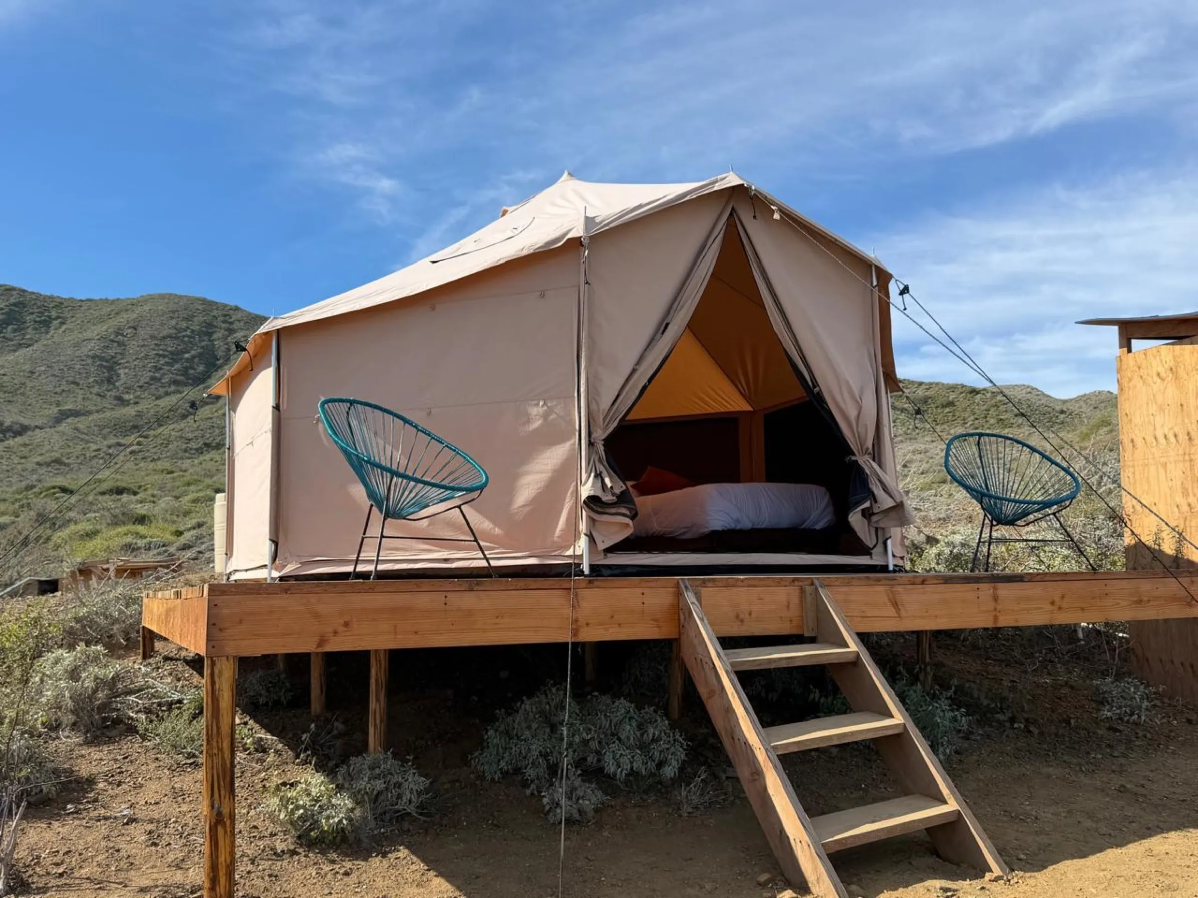 A canvas glamping tent on its wooden deck with two chairs